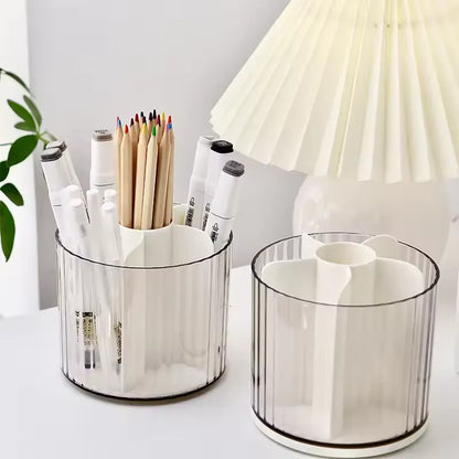 Two white three-compartment desk organizers with clear ribbed plastic sides, shown on a white tabletop with stationery and a pleated lamp in the background.